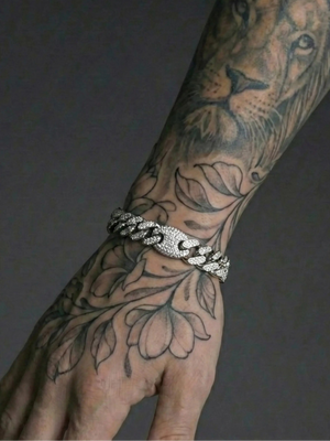 Tattooed arm with intricate designs and a silver bracelet on a dark background