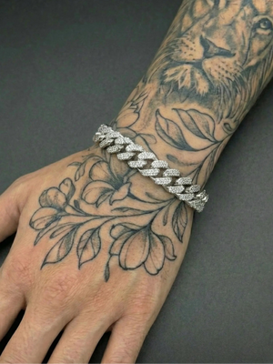 Silver chain bracelet on a wrist with tattoos of a lion and leaves.
