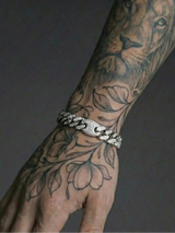 Tattooed arm with intricate designs and a silver bracelet on a dark background