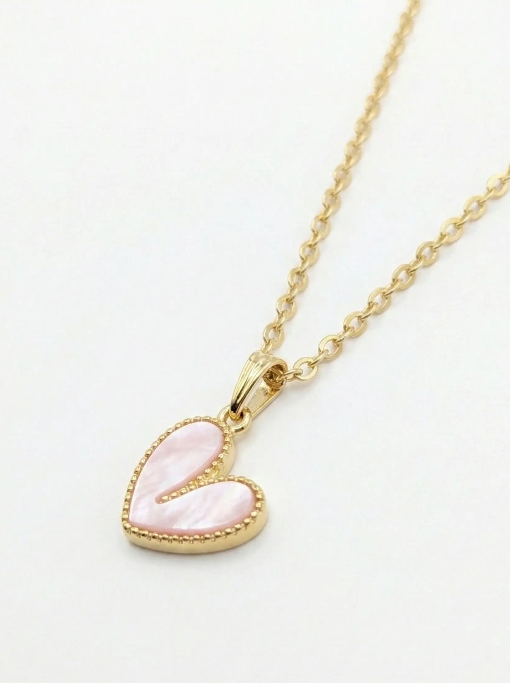 Gold necklace with a pink heart-shaped pendant on a white background