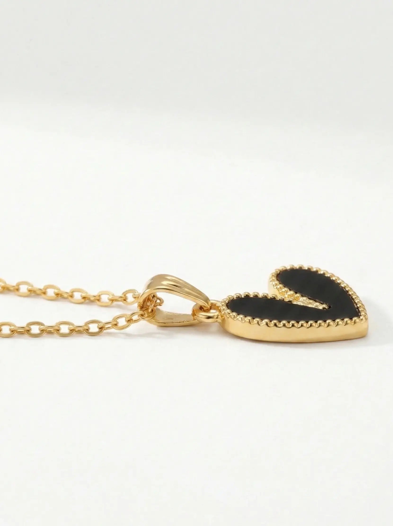 Gold necklace with a black heart-shaped pendant on a white background
